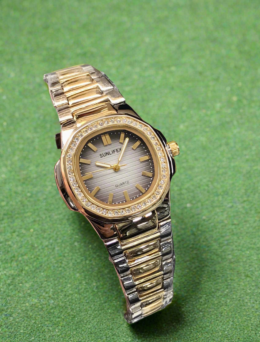 Gold and silver watch held by a hand with a visible brand tag in the background.